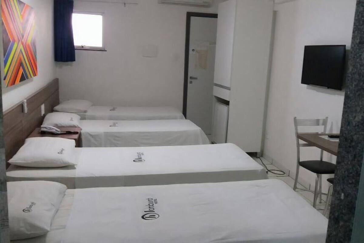 A hotel room with three beds, a TV, a desk, and a chair.