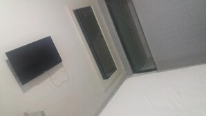A room with a flat-screen TV mounted on the wall, a window, and a door. - Samburá Hotel - Feira de Santana (Feira de Santana)