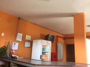 Uma área de recepção com uma geladeira branca, uma pequena TV em cima, um telefone e uma decoração de árvore de Natal.