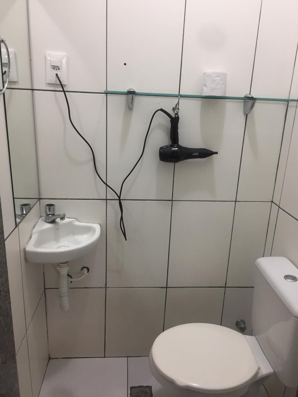 Ein kleines Badezimmer mit einem weißen Waschbecken, einer Toilette und einem an der Wand befestigten Föhn.