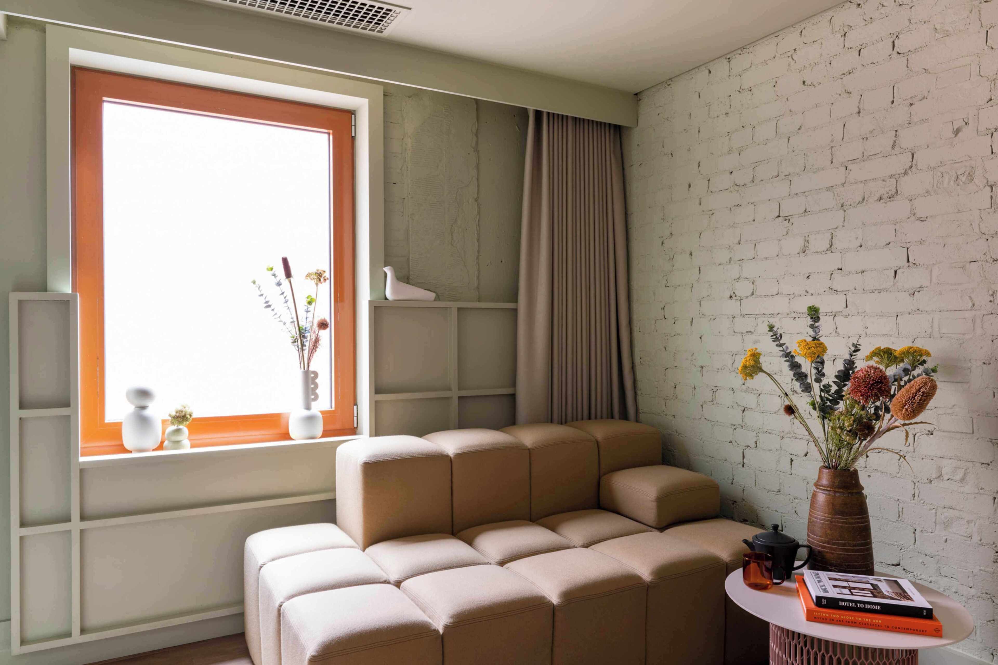 Una sala de estar moderna con un sofá modular, un ventanal con vistas, una mesita con un florero y una pared de ladrillo.