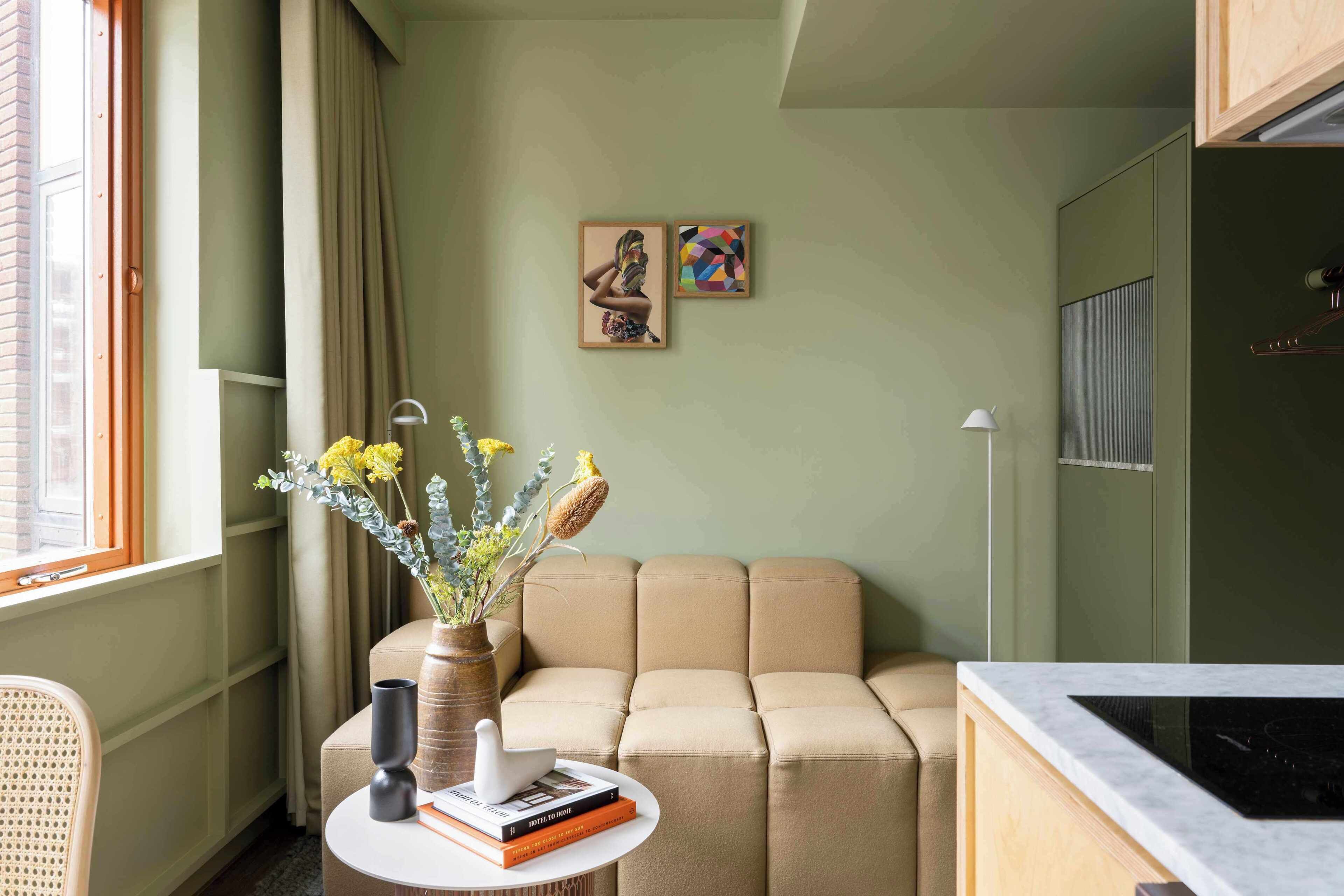 A room with a sofa, a small table with books and a vase, a window with curtains, and two framed pictures on the wall.
