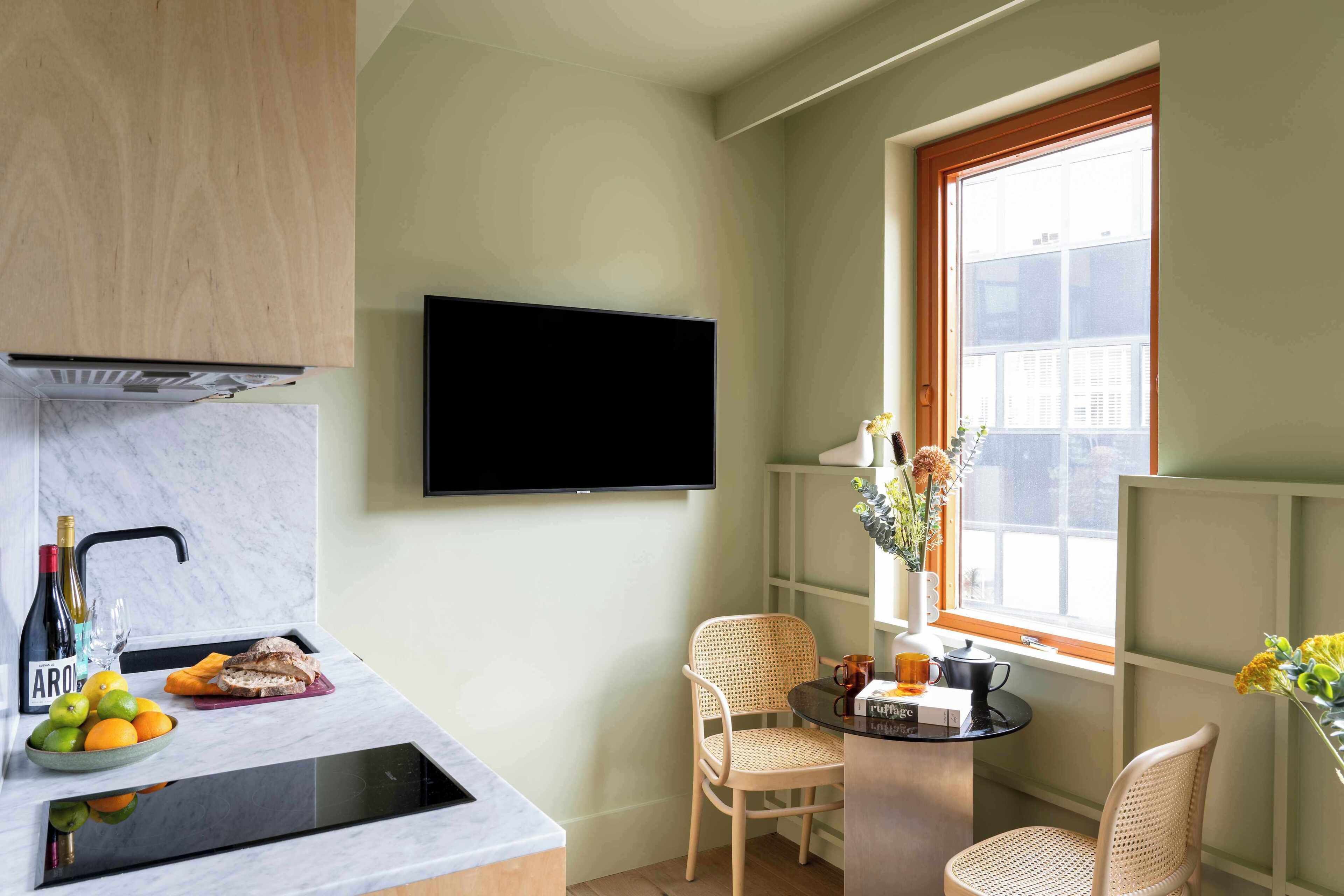 Cocina compacta con televisión de pantalla plana, un lavamanos, una pequeña zona de comedor con sillas y una ventana con vistas.