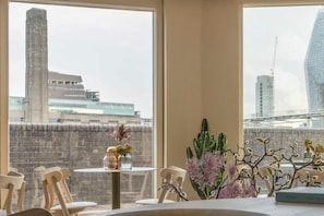 A room with large windows, a brick wall, and a view of a cityscape including a tall building and a construction crane. - Locke At Broken Wharf (London)