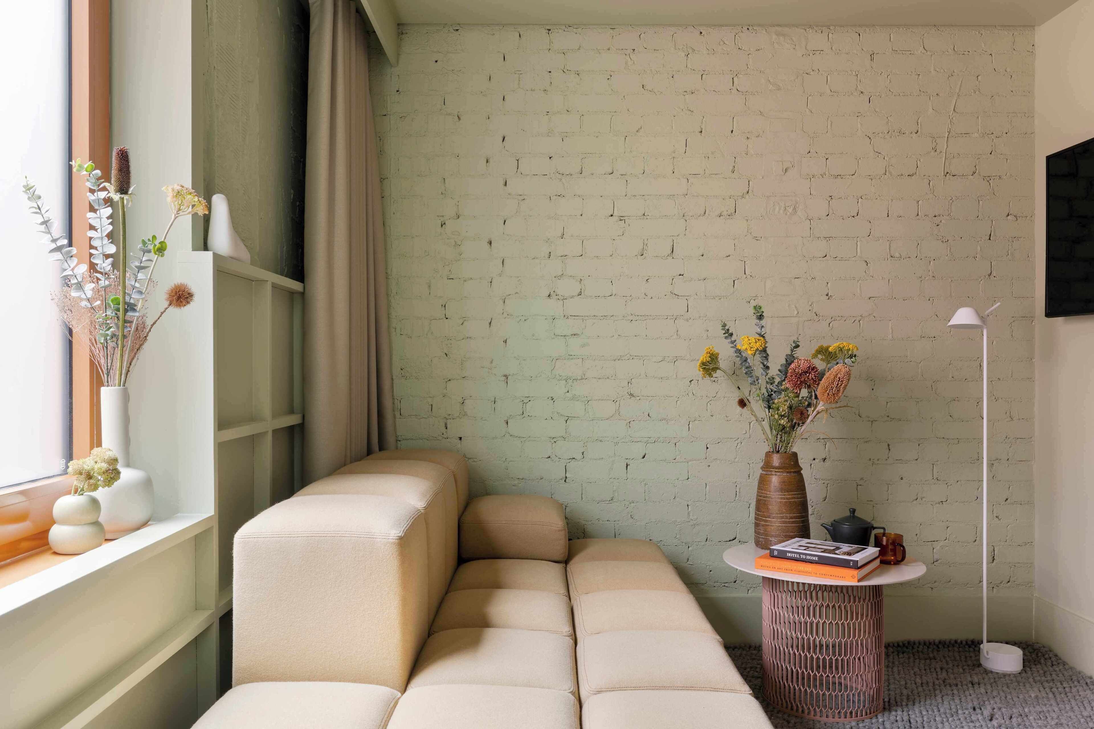 A modern living room with a sofa, a round table with a vase and books, and a brick wall.