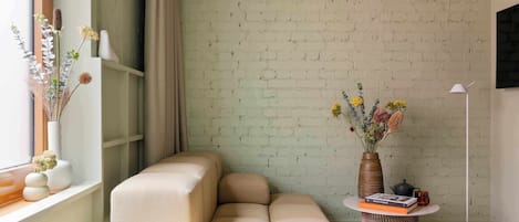 A modern living room with a sofa, a round table with a vase and books, and a brick wall.