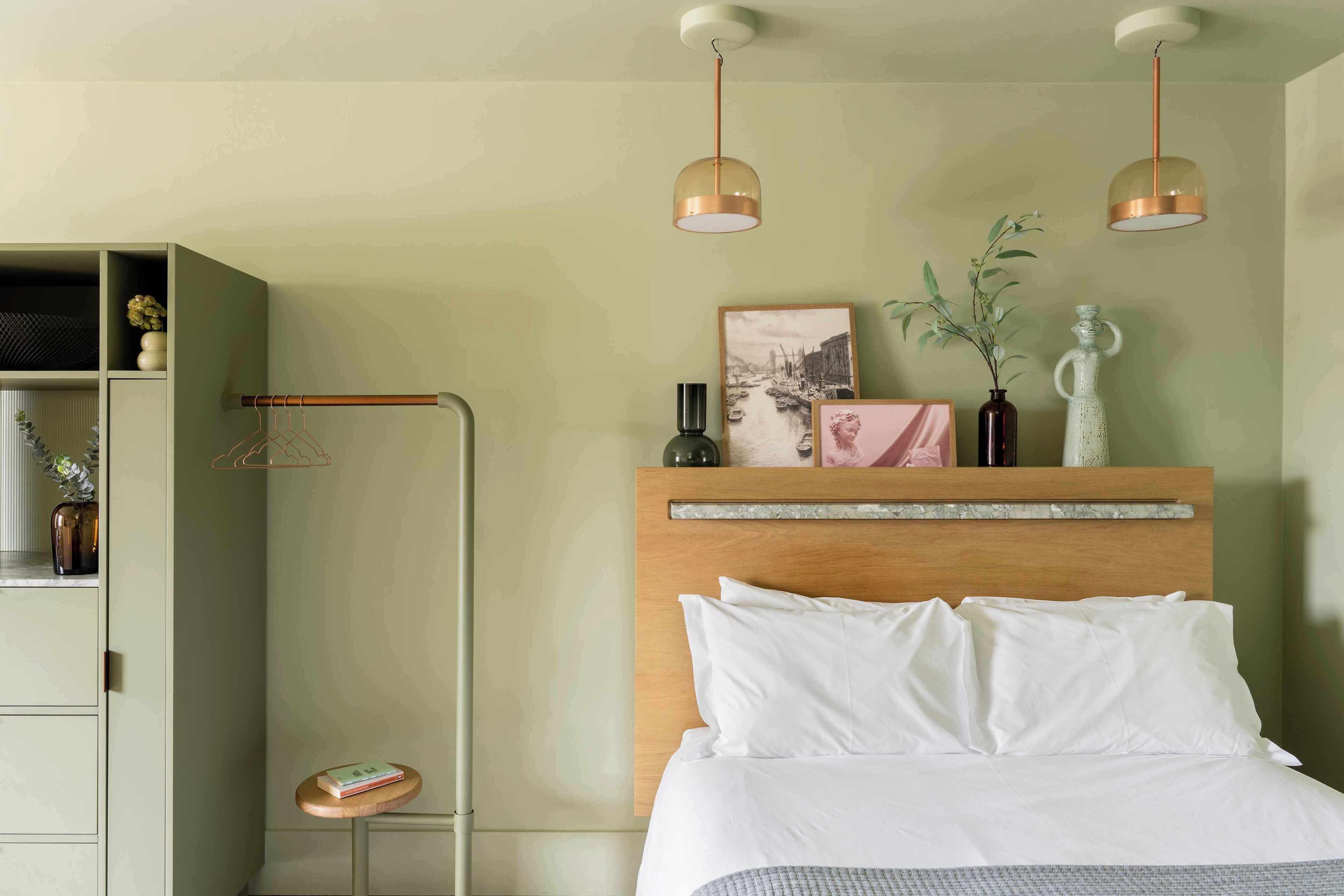 Una habitación de hotel ordenada con cama, una mesita, un armario y dos lámparas colgantes.