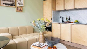 A modern living room with a beige sofa, a round coffee table with books and a vase, and a kitchen area with wooden cabinets and a marble countertop. - Locke At Broken Wharf (London)