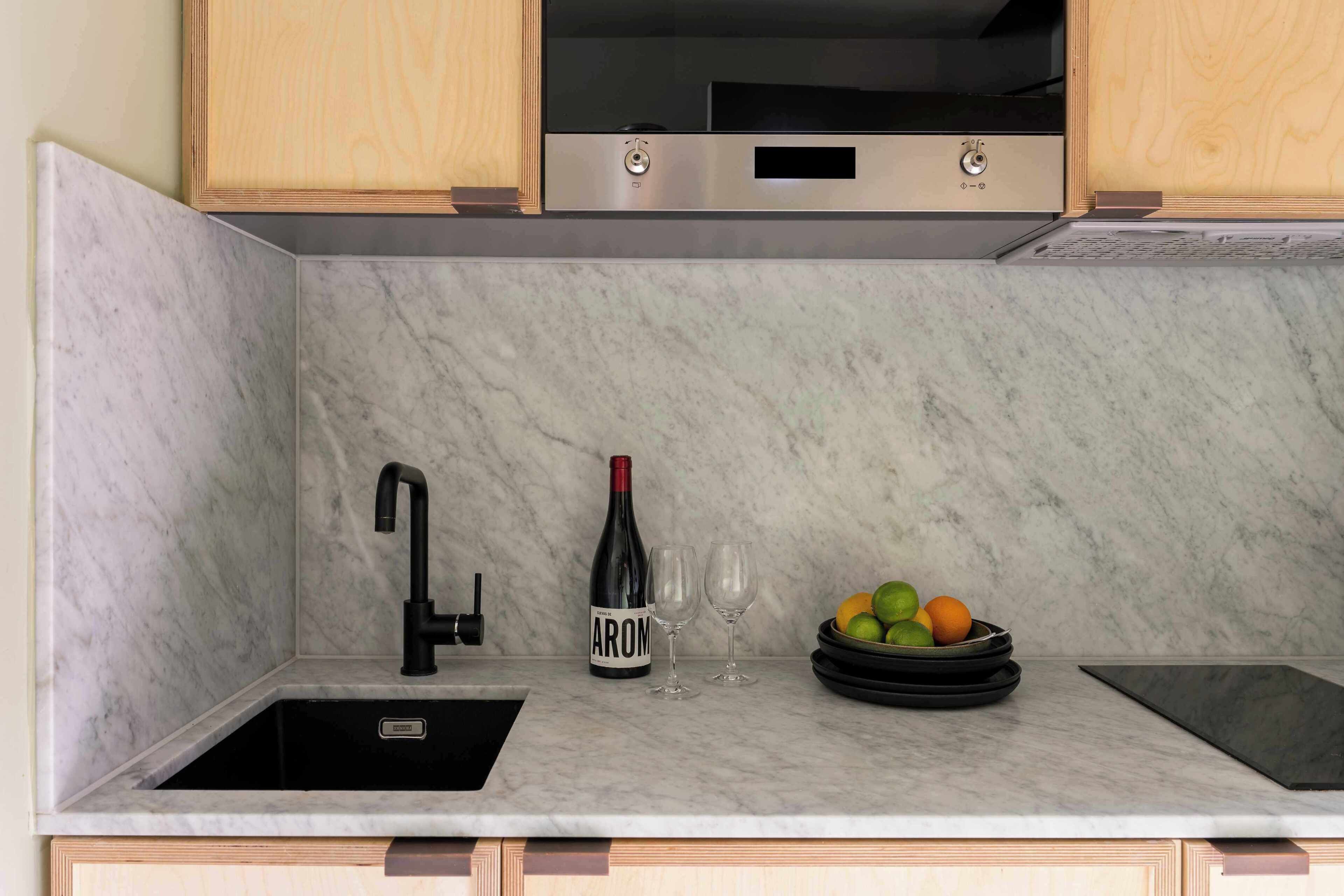 A kitchen with a marble countertop, a wine bottle, two glasses, and a bowl of fruit.