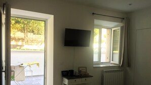 A bedroom with a bed, a TV on the wall, a radiator, and a window with curtains. - B&B MonteCengio (Trieste)