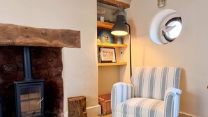Een gezellige kamer met een open haard, een gestreept fauteuil, een lamp en een plank met boeken en decoratieve objecten.