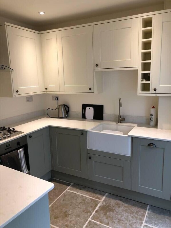 A modern kitchen with grey cabinets, a built-in oven, a sink, and a kettle.