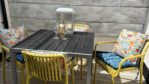 Een terras met een tafel, stoelen, een fles wijn en een lantaarn.