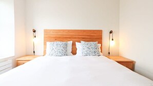 Een slaapkamer met een houten hoofdbord, wit beddengoed, twee bedlampen en een nachtkastje.