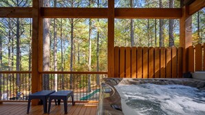 A wooden deck with a hot tub, two tables, and a slide, overlooking a forest.