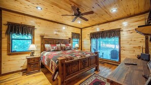 Quarto de cabana de madeira com cama, mesa de cabeceira, escrivaninha e ventilador de teto.