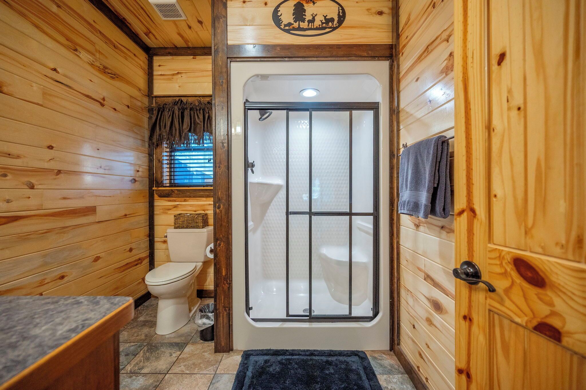 A wooden cabin bathroom with a toilet, shower, and sink.