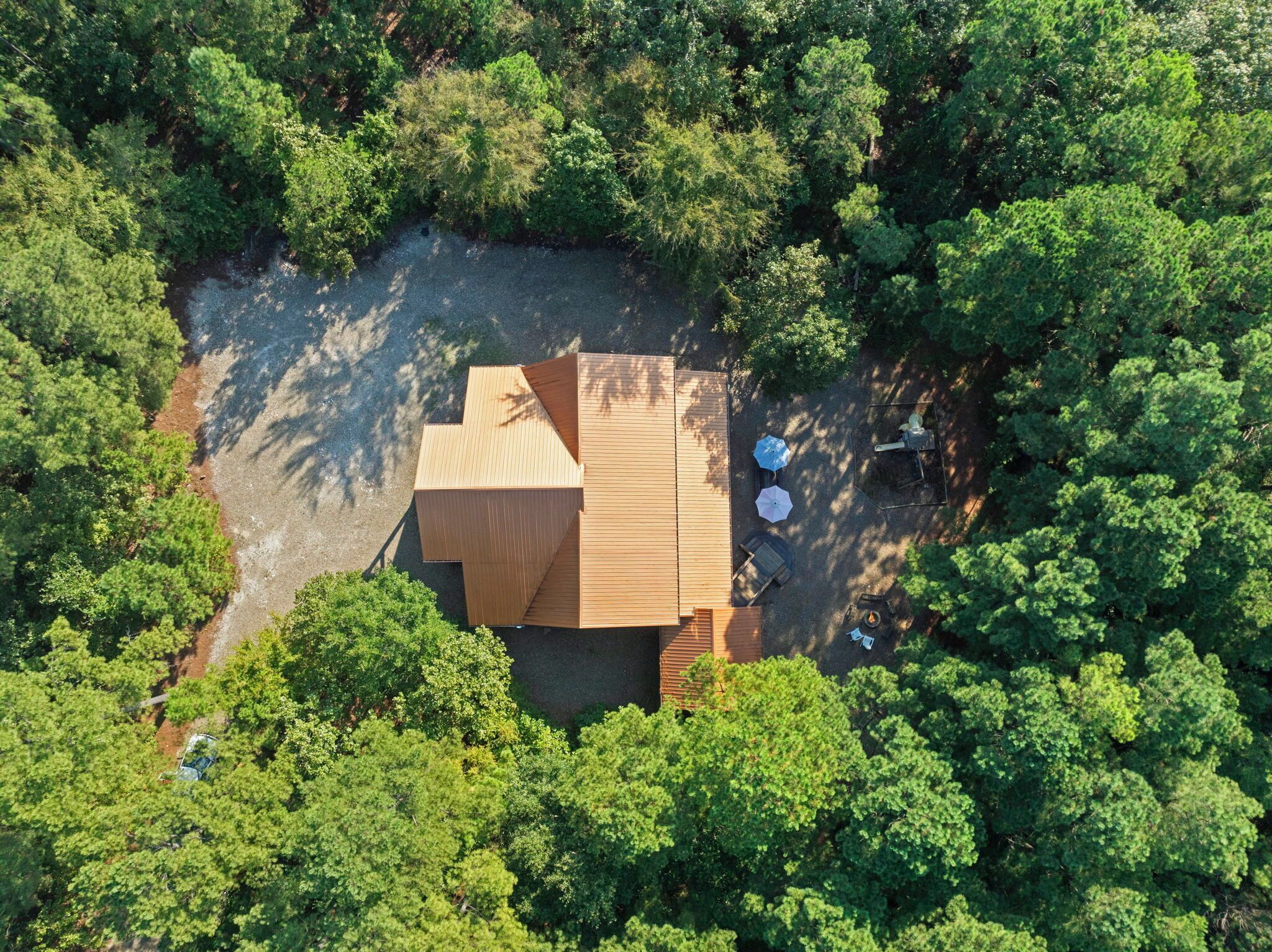 Vue aérienne d’un chalet en bois entouré d’une forêt dense.