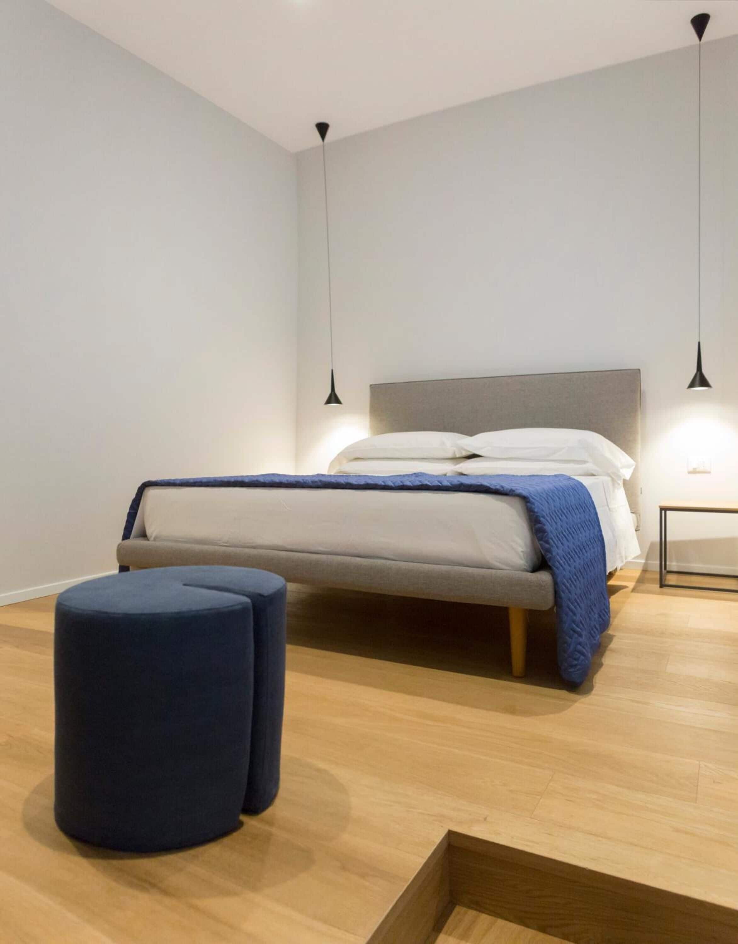 A modern bedroom with a bed, two bedside tables, and a round ottoman.