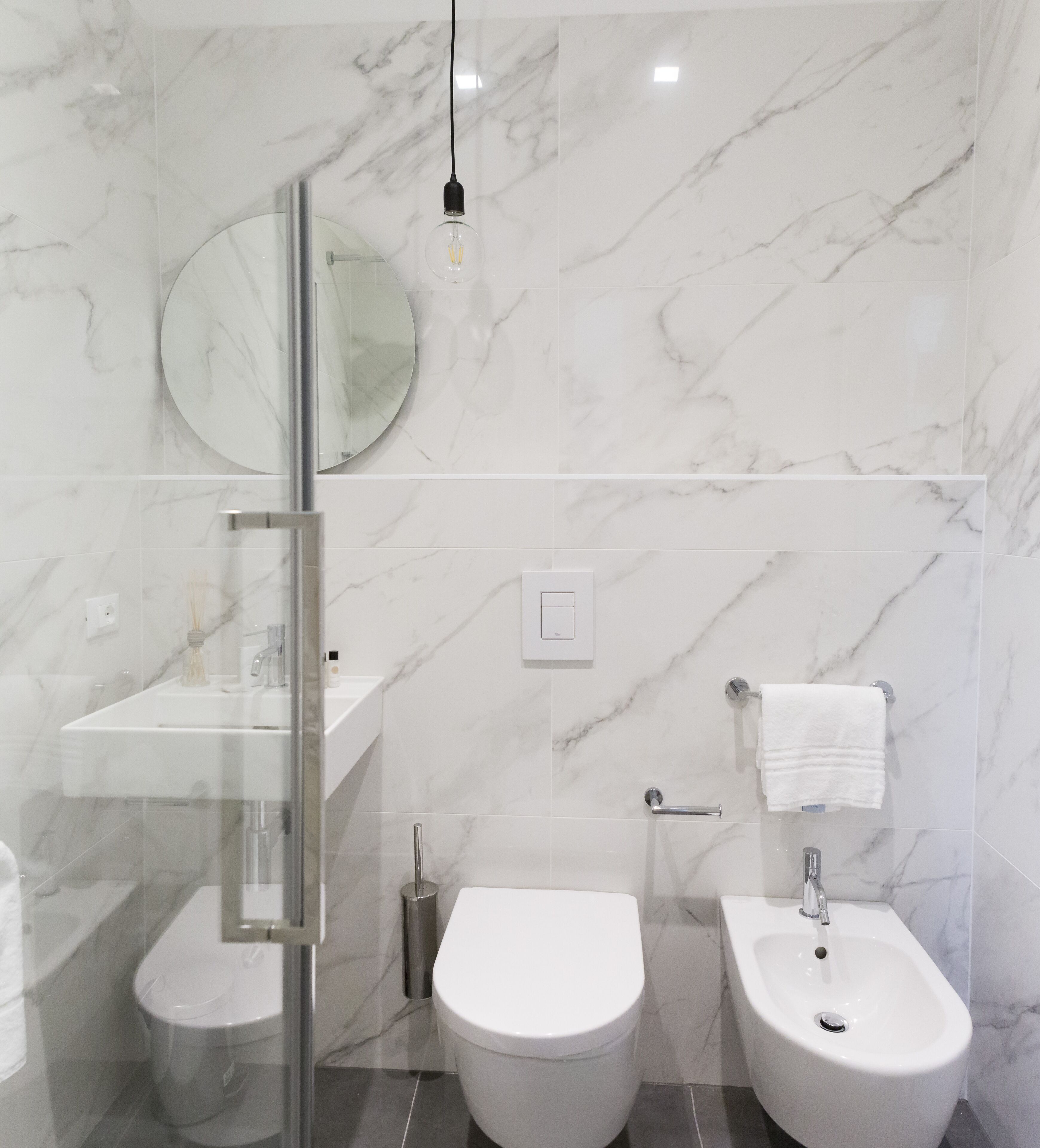 Ein modernes Badezimmer mit einer Duschkabine aus Glas, einem runden Spiegel, einer Toilette und einem Bidet.