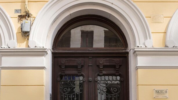 A yellow building with a dark brown door featuring ornate metalwork and a decorative arch above it. - Trieste 411 e Trieste 411 II (Rooms & Apartments) (Trieste)