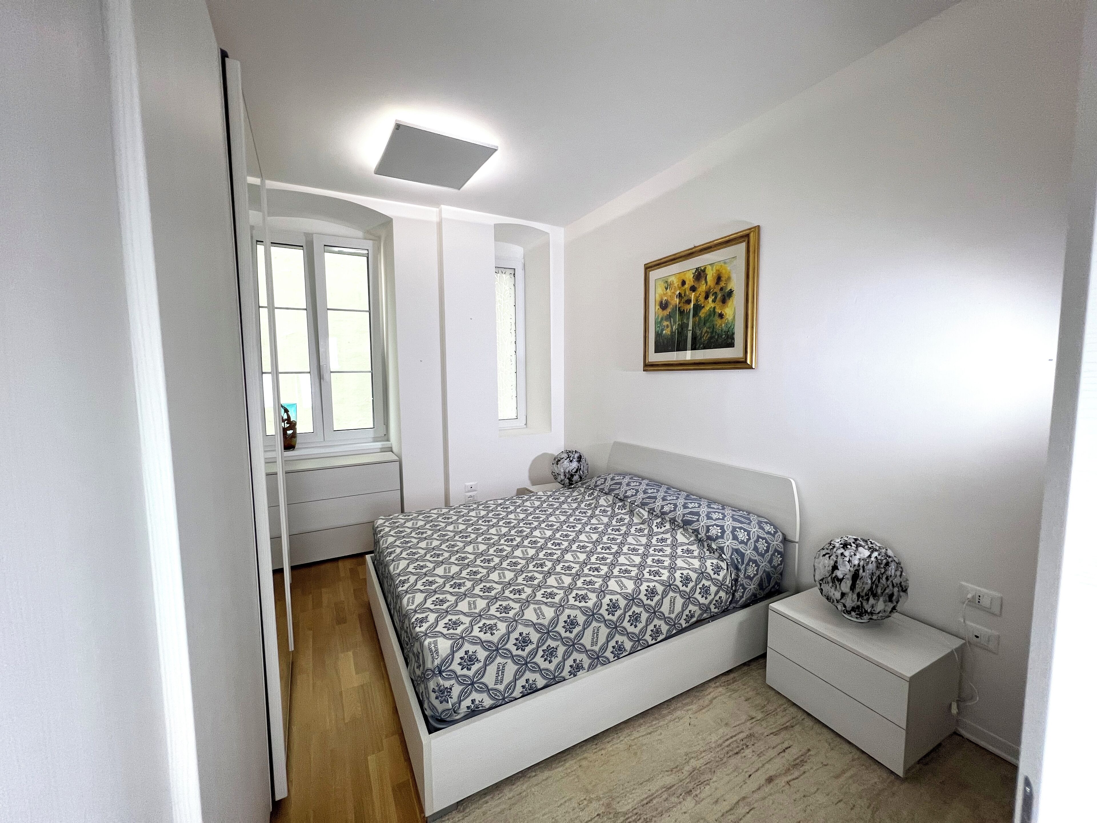 A bedroom with a bed, a nightstand, a window, and a painting on the wall.