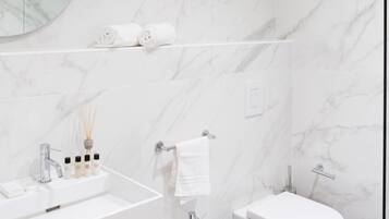 Un baño moderno con pared de mármol, espejo redondo, lavamanos blanco, bidé y toallero.