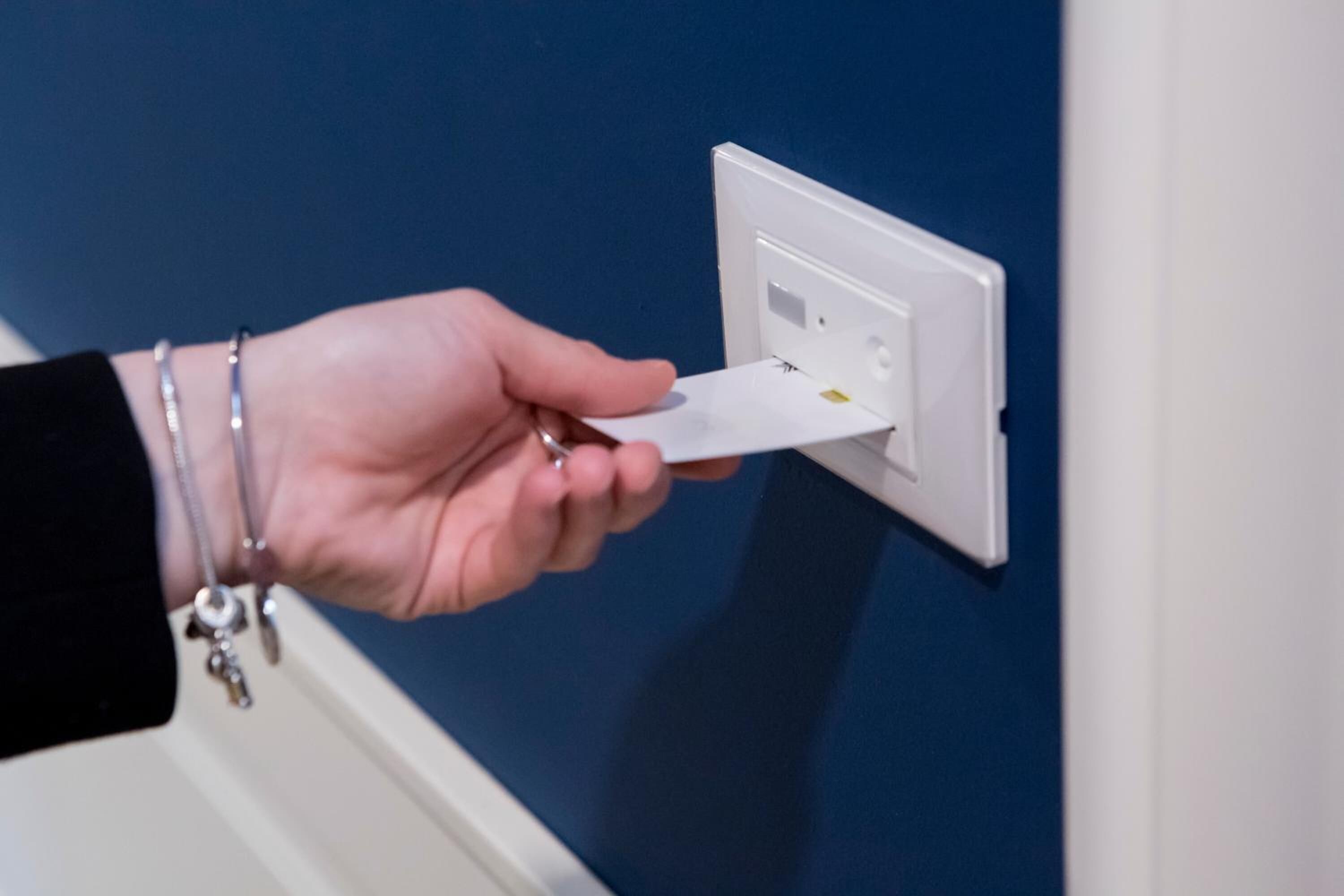 Una mano sosteniendo una tarjeta cerca de un enchufe blanco en una pared azul.
