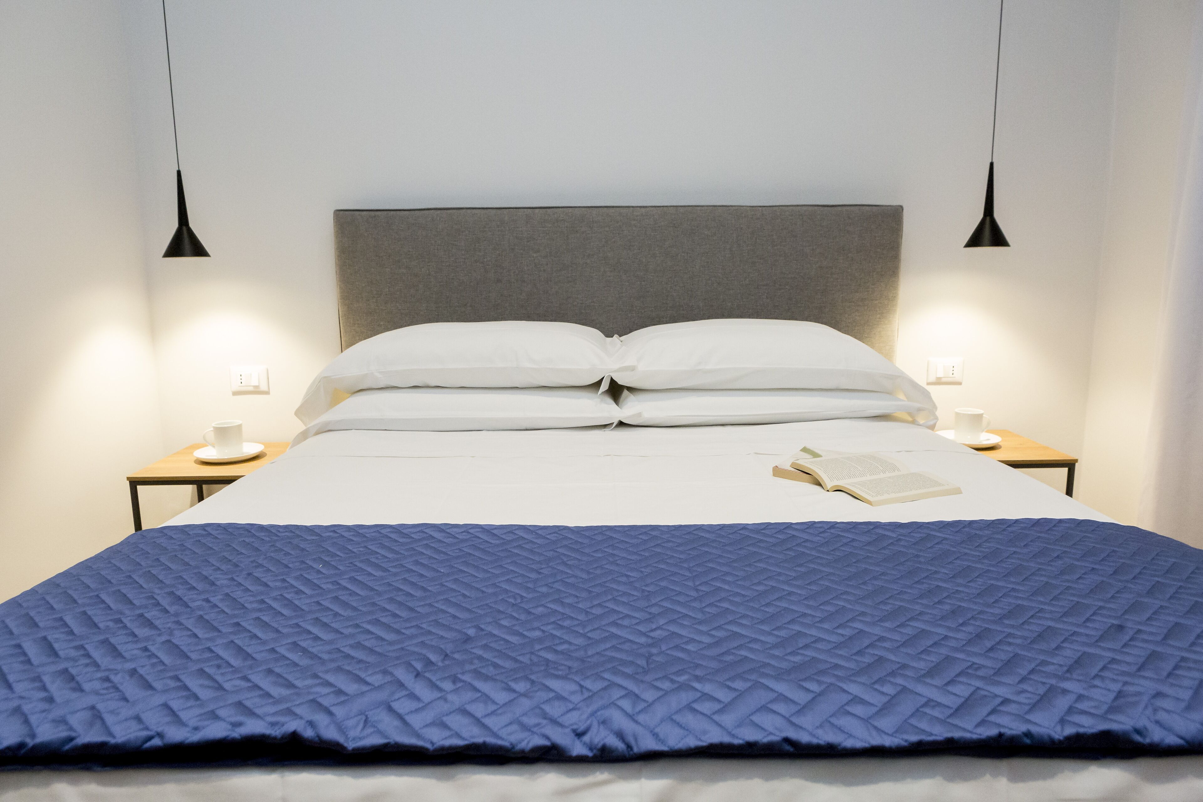Un lit bien fait, recouvert d’une couette bleue, deux tables de chevet avec des lampes et un livre posé sur le lit.