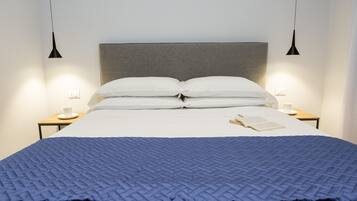 Un lit bien fait, recouvert d’une couette bleue, deux tables de chevet avec des lampes et un livre posé sur le lit.