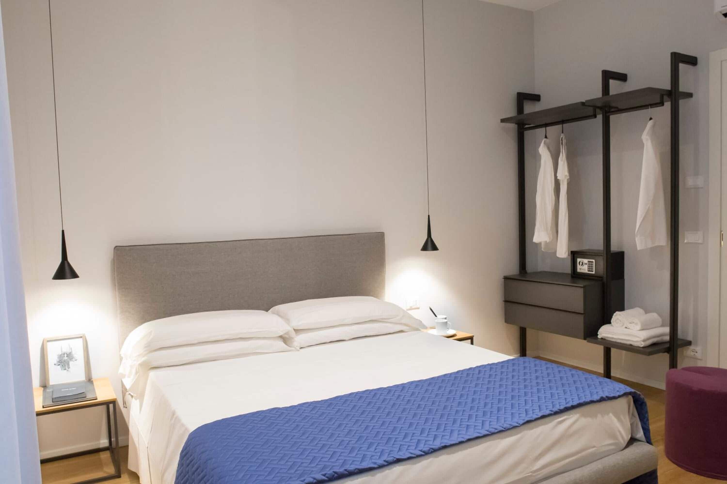 Een moderne slaapkamer met een groot bed, nachtkastjes, een garderobe en hangende kleding.