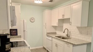 Una cocina con armarios blancos, encimera de granito, pileta de acero inoxidable y cafetera.