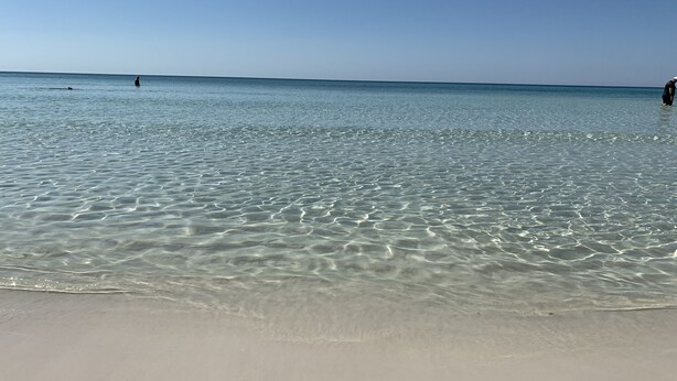 Una playa con aguas poco profundas y cristalinas y una orilla arenosa.