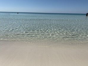 A beach with clear shallow water and a sandy shore. - Cute Condo Steps from Beach (Miramar Beach)