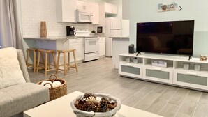 Una sala de estar moderna con televisor, sofá y una zona de comedor con taburetes.