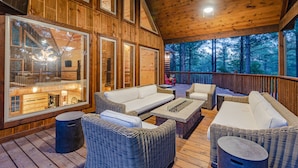 A wooden deck with wicker furniture, large windows, and a view of the forest. - Boomerang Cabin | Large Family Retreat Near Broken Bow Lake (Broken Bow)