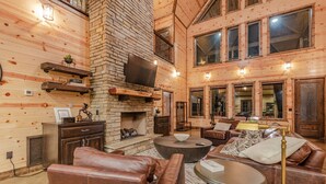 A cozy log cabin interior with a fireplace, leather furniture, and a television mounted on the wall. - Boomerang Cabin | Large Family Retreat Near Broken Bow Lake (Broken Bow)