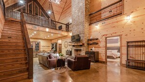 A spacious living area with a high ceiling, wooden walls, a fireplace, and a television mounted on the wall. - Boomerang Cabin | Large Family Retreat Near Broken Bow Lake (Broken Bow)