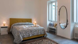 Ein Schlafzimmer mit Bett, Nachttischlampen, einem großen Spiegel, einem Fenster und einer Heizung.