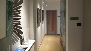 Un couloir avec un comptoir d’accueil, des œuvres d’art encadrées accrochées aux murs, une porte ornée d’un rideau à rayures et un panneau indiquant le numéro de la chambre 5.