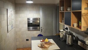 Une cuisine équipée d’un four encastré, d’une étagère en bois où sont rangés de la vaisselle, et d’une machine à café posée sur le plan de travail.