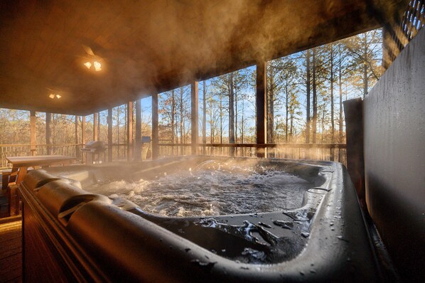 A hot tub with steam rising, surrounded by wooden deck and tall trees.