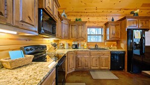 A kitchen with wooden cabinets, a stove, microwave, refrigerator, and a dishwasher. - Bryce’s Crossroad | Family Cabin Near Broken Bow Lake (Broken Bow)