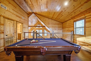 A wooden interior with a pool table, wooden walls, and a balcony.