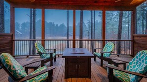 Una terraza techada al aire libre con muebles de madera y una parrilla, con vistas a un área boscosa.
