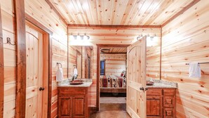 Interior de una cabaña de madera con baño que incluye un lavamanos, espejo y toallero.