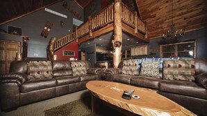 Ein gemütliches Wohnzimmer mit einer großen Ledersofa-Garnitur, einem Holztisch und einer rustikalen Holztreppe.