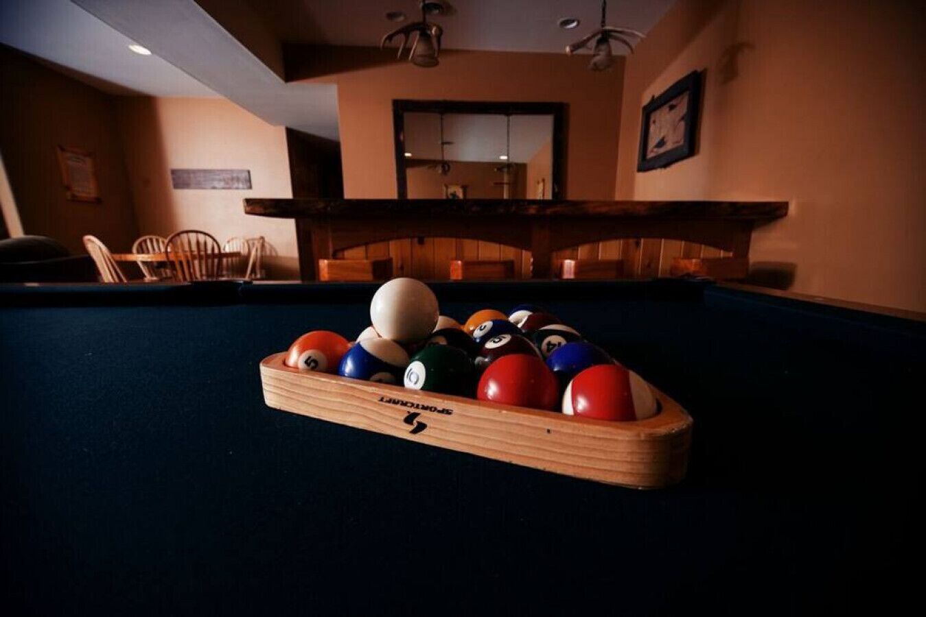 A pool table with a wooden edge and a pool cue rack.