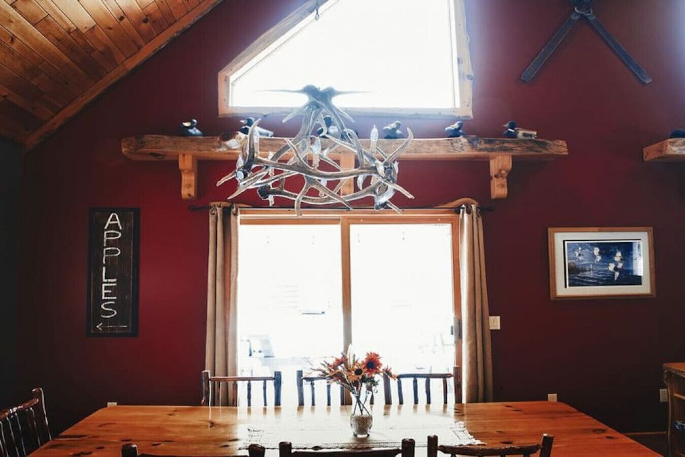 A dining area with a wooden table, chairs, a chandelier, a window, and a sign on the wall.