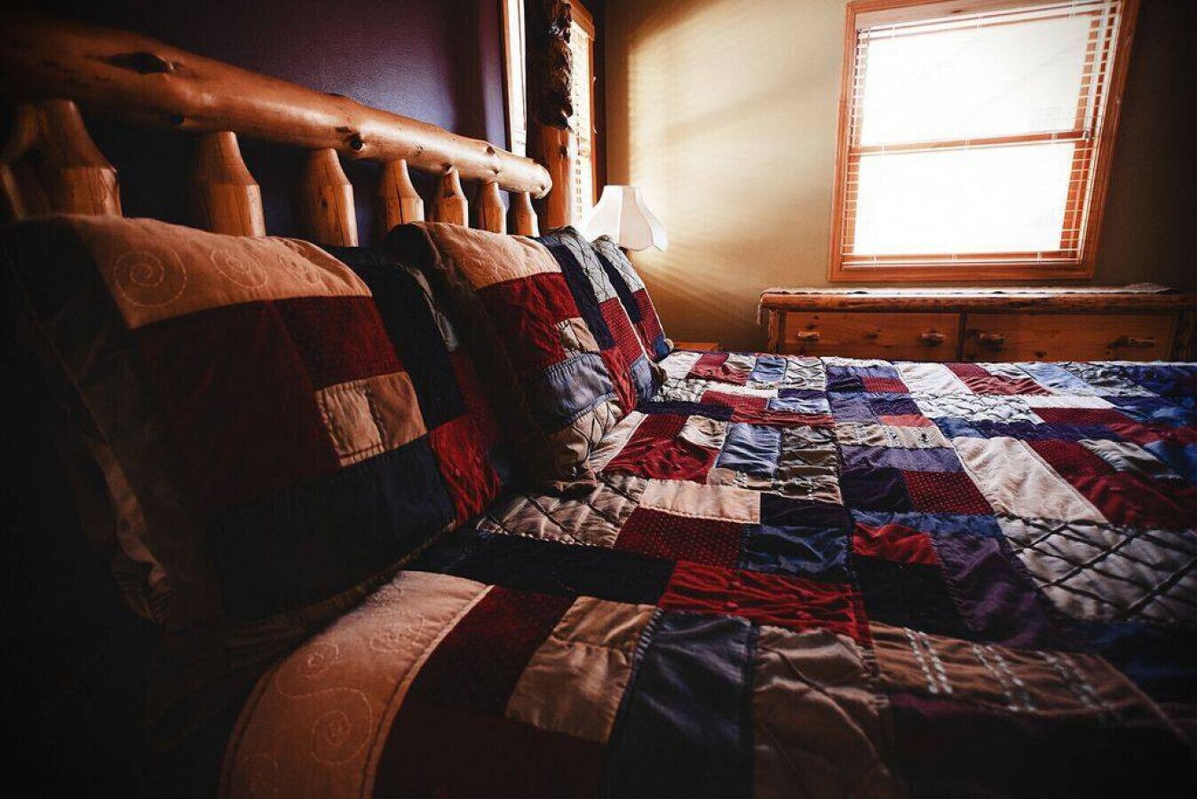 A bed with a quilted headboard and a window with blinds.